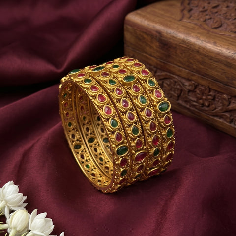 Gold bracelet with gemstones on a maroon fabric background