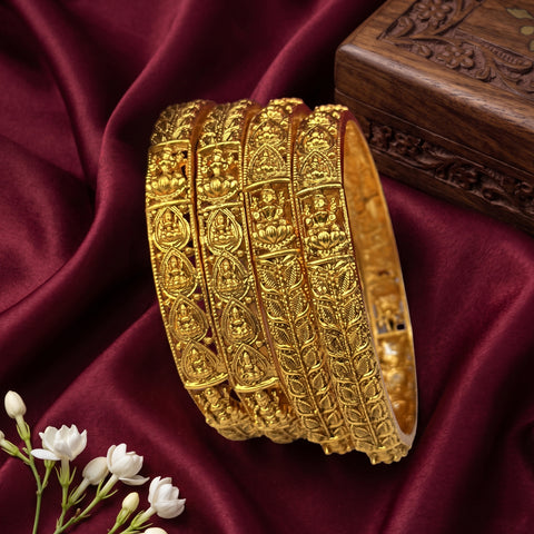 Three gold bangles with intricate designs on a maroon fabric background