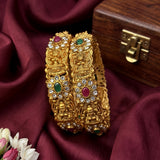Gold bangles with gemstones on a maroon fabric background