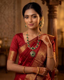 A woman wearing a red and gold traditional Indian saree with a matching red and gold necklace, earrings, and bangles, posed in an ornate indoor setting.