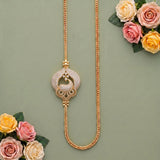 A gold-toned necklace with a decorative circular pendant covered in small clear stones, displayed on a muted green background with pink and cream roses in the corners.