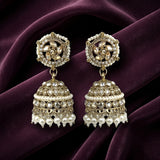 A pair of ornate Indian jhumka earrings with gold-plated filigree, white faux pearls, and clear rhinestones, displayed on a draped deep purple velvet fabric.