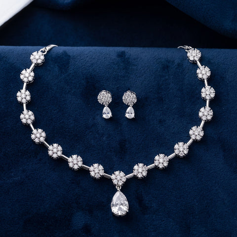 Silver-tone jewelry set featuring a necklace with floral clusters and a teardrop pendant, plus matching stud earrings, displayed on a dark blue velvet surface.