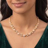 A close-up of a woman wearing a delicate gold necklace with pavé-set clear stones and small diamond-shaped accents, paired with a dark green velvet top.