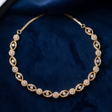 A gold chain necklace with repeating oval and floral motifs set with clear stones, displayed on a dark blue velvet fabric background.