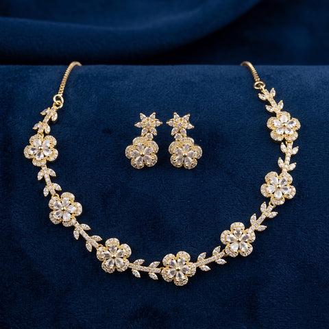 Gold floral jewelry set with a matching necklace and earrings, featuring clear rhinestone-like flowers and leaves, displayed on a dark blue velvet fabric background.