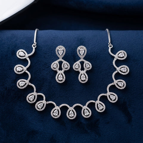 Silver-tone jewelry set featuring a necklace and matching earrings with teardrop-shaped clear stones, displayed on a dark navy velvet surface.