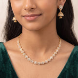 A close-up of a model wearing a gold necklace with circular pavé-set clear stones and matching dangling earrings, paired with a dark green velvet top.