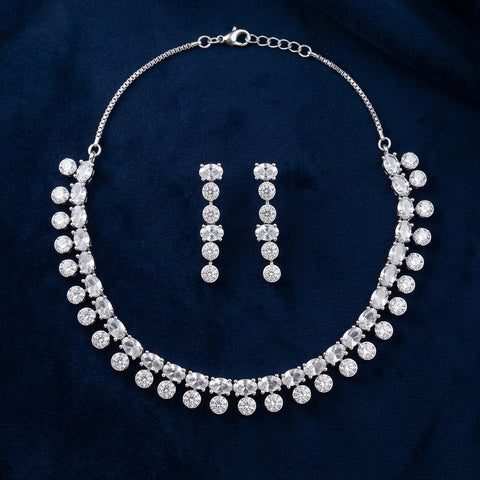 A silver-tone jewelry set featuring a collar-style necklace and matching drop earrings, both adorned with clear round and square-cut rhinestones, displayed on a dark navy blue velvet fabric background.