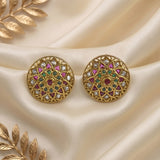 A pair of gold-plated Indian Kundan earrings with intricate mandala designs, featuring pink, green, and white stones, displayed on a cream satin fabric with gold leaf accents.