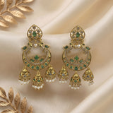 A pair of ornate gold-toned chandelier earrings with green stone accents and dangling pearl-like beads, displayed on draped cream satin fabric with decorative gold leaves.