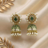 A pair of ornate gold and green jhumka earrings with white pearl accents, displayed on a beige satin fabric background with decorative gold leaf elements.