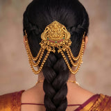 A close-up back view of a woman wearing an ornate gold traditional hair ornament (hair pin) with hanging beaded chains, styled with a deep side braid.