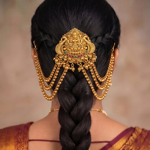 A close-up back view of a woman wearing an ornate gold traditional hair ornament (hair pin) with hanging beaded chains, styled with a deep side braid.