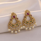 A pair of ornate gold-toned traditional Indian chandbali earrings with red, green, and white stones, displayed on a soft white fabric background.