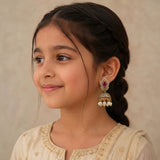 A young girl with dark hair in a braid wearing a traditional Indian outfit and a gold-toned jhumka earring with a pink stone and white pearls, shown in a close-up portrait.