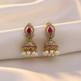 A pair of gold-plated Indian jhumka earrings with teardrop-shaped pink gemstones, small green accent stones, clear rhinestones, and dangling white faux pearls, displayed on a cream satin fabric.