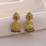 A pair of ornate gold-toned Indian jhumka earrings with red and green stone accents, displayed on a soft white fabric background.