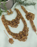 An ornate gold-toned traditional jewelry set arranged on a pale green fabric backdrop, including a necklace, matching earrings, a bracelet, and a dangling pendant. The pieces are decorated with intricate filigree, beadwork, and small multicolored stone accents.