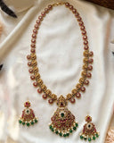 Gold-toned Indian ethnic jewelry set featuring a choker necklace and matching earrings, embellished with red stones, green stones, and white faux pearls, displayed on a draped cream satin fabric.