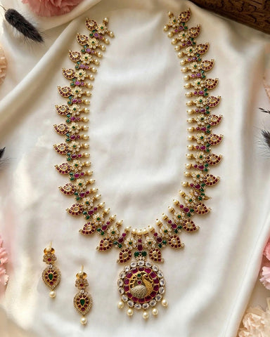 Gold-plated Indian traditional jewelry set featuring a necklace and matching earrings, embellished with white pearls, red stones, and green stones, displayed on a white satin fabric.