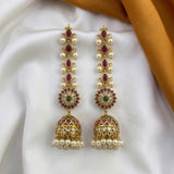A pair of gold-plated Indian chandelier earrings with white faux pearls, pink enamel, and green and white stones, displayed on a white satin fabric with a gold-colored ribbon in the background.