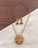Gold-toned necklace and matching earrings with ornate pendant details, displayed on a cream fabric surface over a dark wood background.