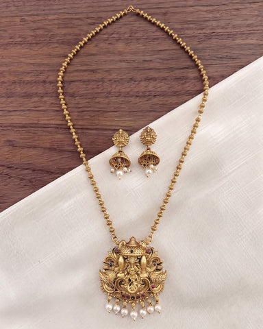Gold-toned necklace and matching earrings with ornate pendant details, displayed on a cream fabric surface over a dark wood background.