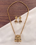 Gold-toned necklace and matching earrings set with a detailed pendant featuring small colorful stones and white pearl drops, displayed on a white fabric surface over a dark wood background.