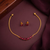 Gold-tone necklace and matching stud earrings with red gemstone accents, arranged on a dark burgundy fabric surface with a wooden edge visible in the corner.