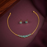 Gold-tone jewelry set featuring a necklace and matching stud earrings with light blue rectangular gemstones, arranged on a dark burgundy fabric surface.