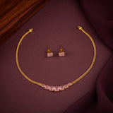 Gold-tone necklace and matching stud earrings with pale pink rectangular stones, arranged on a dark burgundy fabric surface.