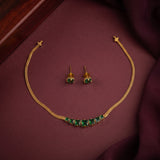 Gold jewelry set featuring a necklace and matching earrings with green stone accents, displayed on a dark burgundy fabric background.