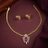 Gold-tone necklace and matching stud earrings set with a central oval pink gemstone and clear crystal detailing, displayed on a dark burgundy fabric background.