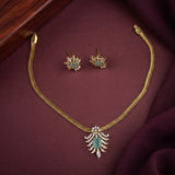 Gold jewelry set featuring a necklace and matching earrings with light green stone accents and clear rhinestone details, displayed on a dark burgundy fabric background.
