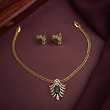 Gold-tone jewelry set featuring a chain necklace with a decorative leaf-shaped pendant containing a green oval stone and clear stones, accompanied by matching stud earrings, displayed on a dark burgundy fabric background.