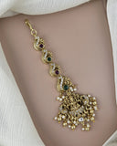 Gold anklet with green and red gemstones on a person's ankle against a white background