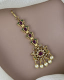 Gold necklace with red and green gemstones and pearl drops on a plain background