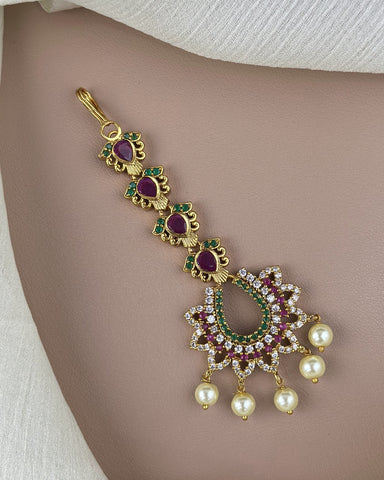 Gold necklace with red and green gemstones and pearl pendants on a beige background