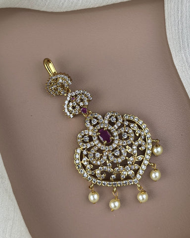 Ornate gold pendant with pearls and a red gemstone on a beige background
