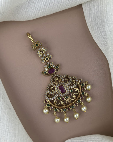 Decorative gold pendant with pearls and gemstones on a neutral background