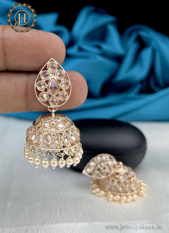 A pair of gold-plated kundan with pearl studded earrings against a blue background, with the brand mark visible on the image.
